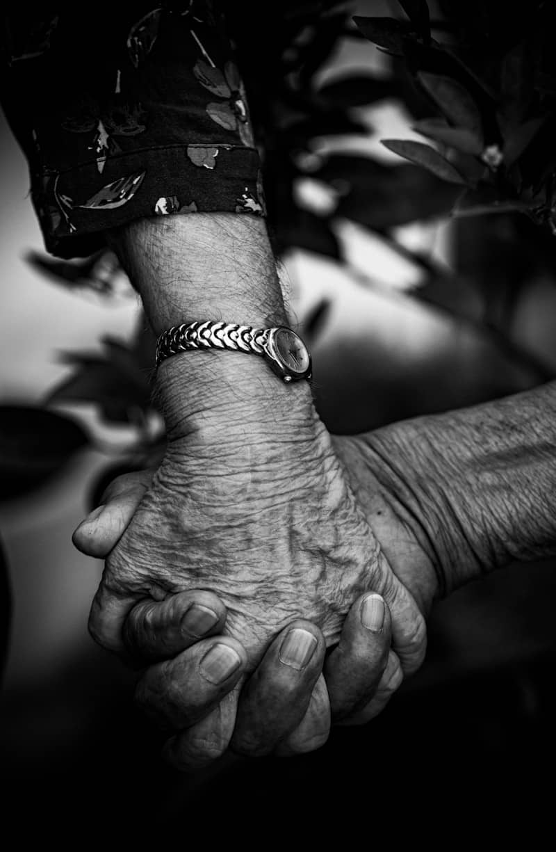 Two elderly hands clasped together, showing connection.