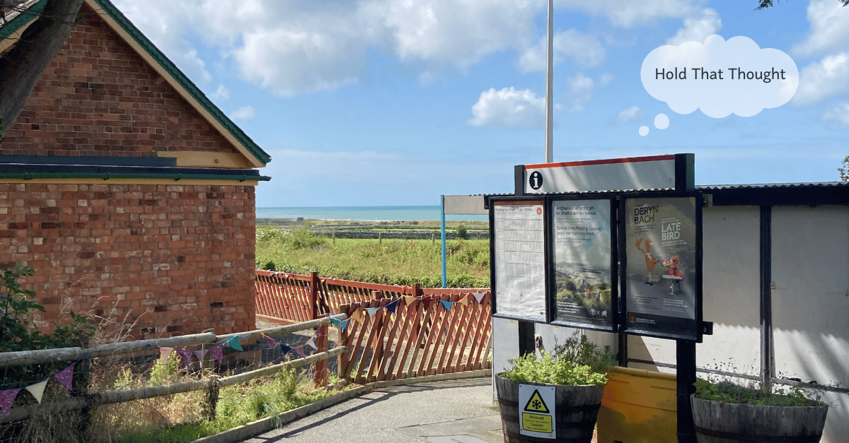 A very small train station with a view of the sea on a sunny day in Wales.