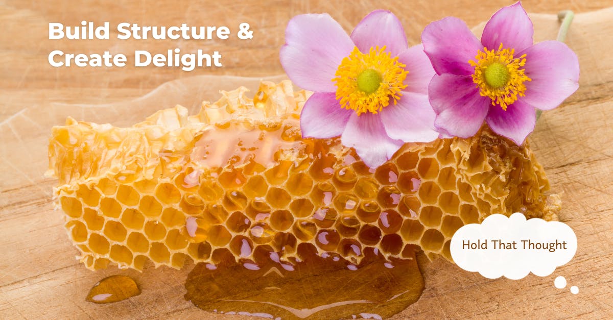 A gorgeous piece of honeycomb oozes honey. Two pink-purple flowers sit on top.