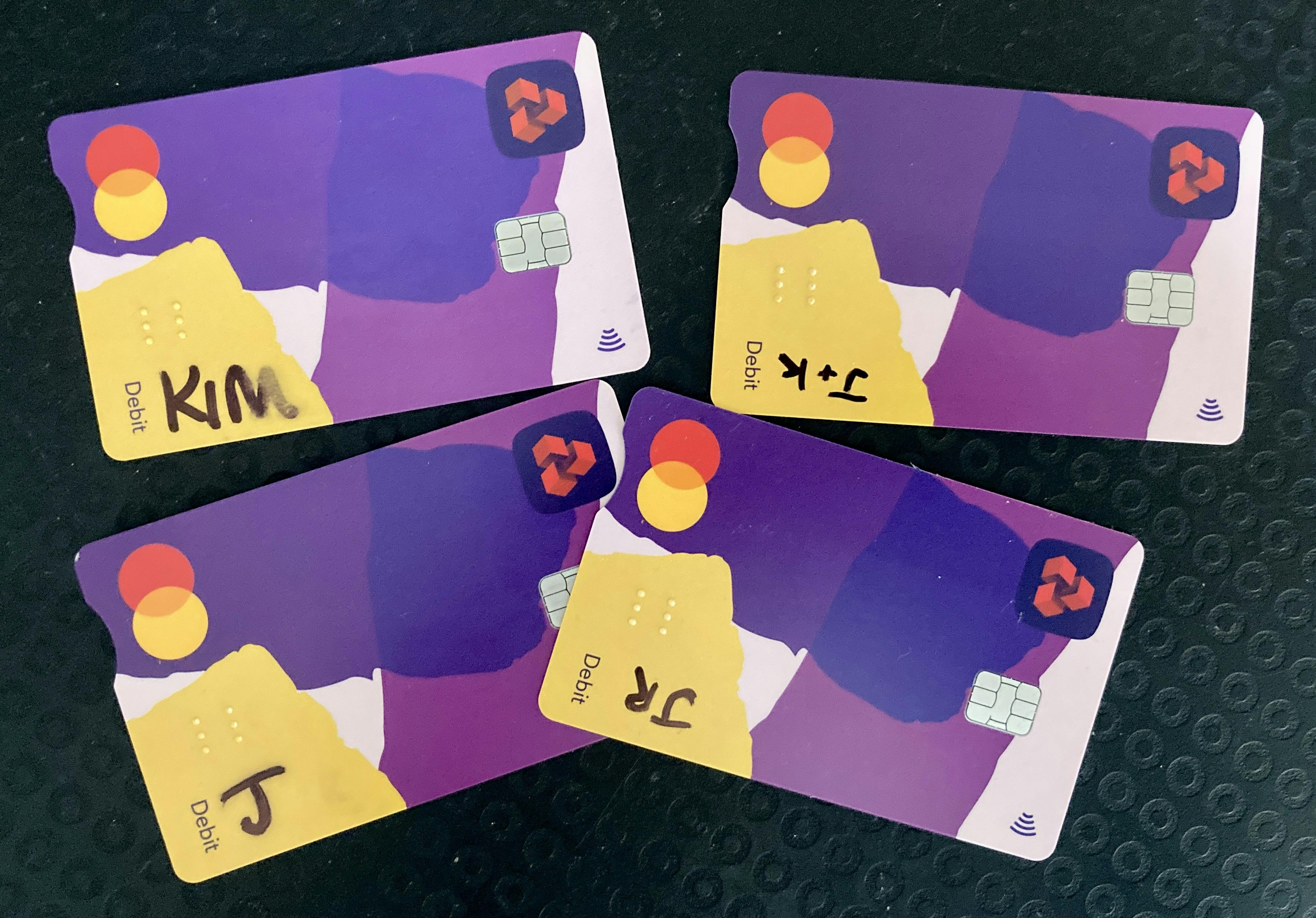 Four identical Natwest bank cards against a black background. Each card has initials in the bottom left corner, written in sharpie pen.