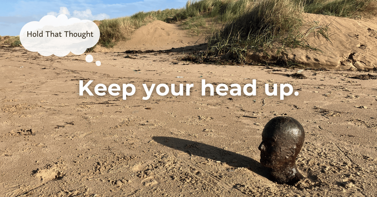 A beach with an iron statue of Anthony Gormley, buried up to his neck.