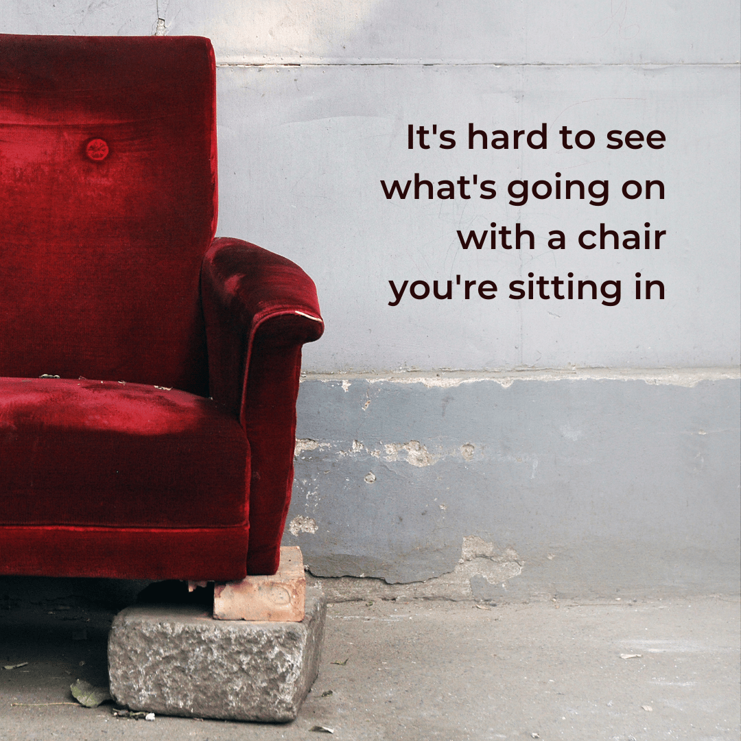 A red velvet chair against a concrete wall. The front leg is supported by blocks.