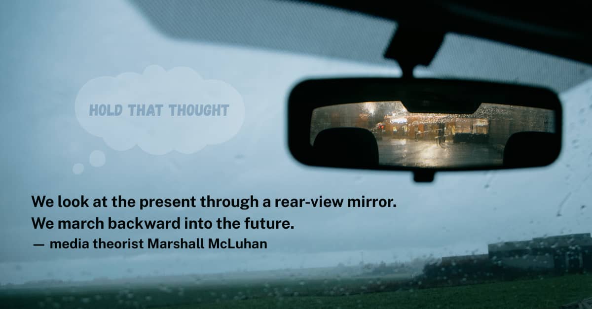 Perspective from inside a car on a gloomy day, with focus on rearview mirror. Quote by Marshall McLuhan. 