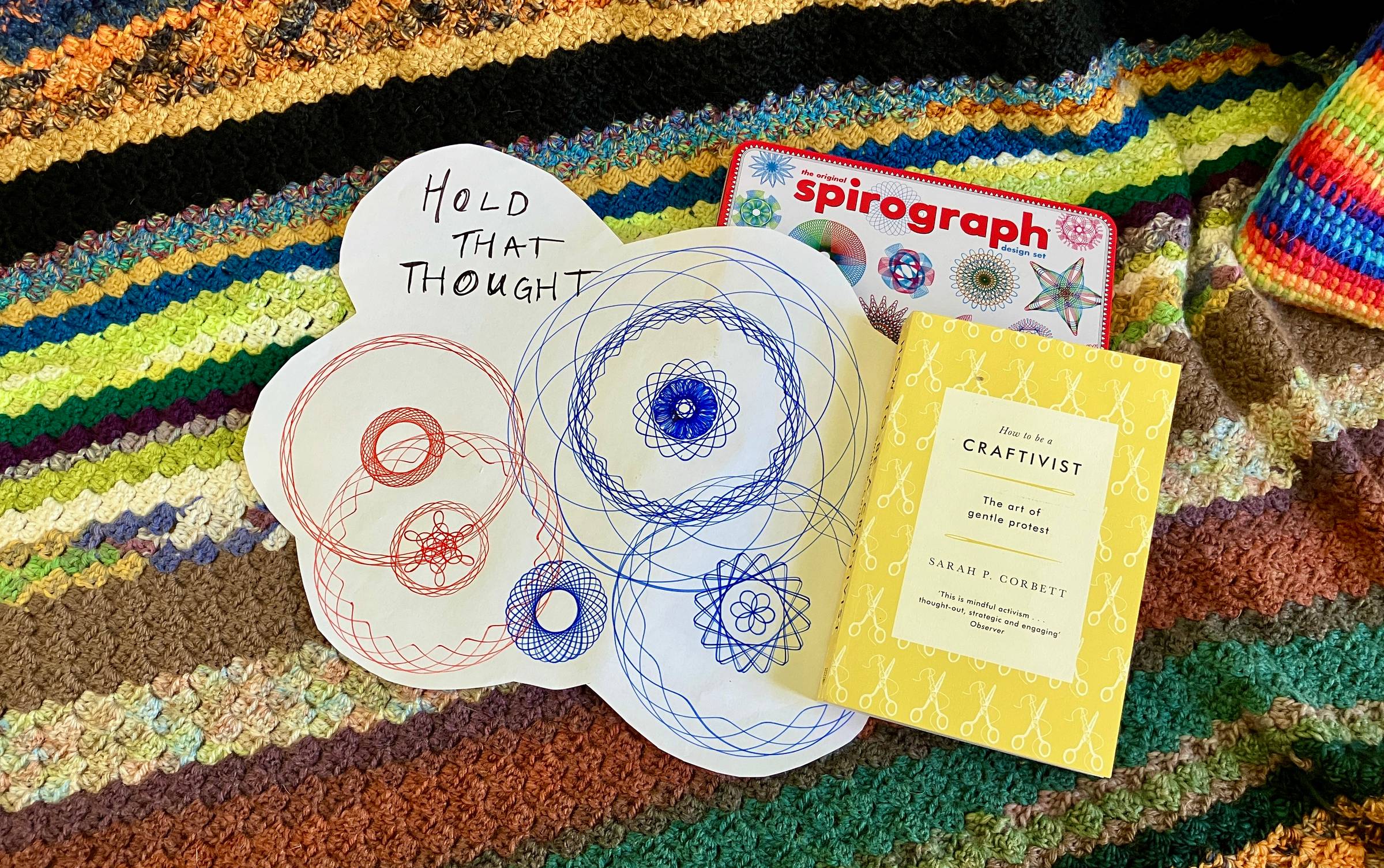 A spirograph and Craftivist book against a colourful crochet blanket.