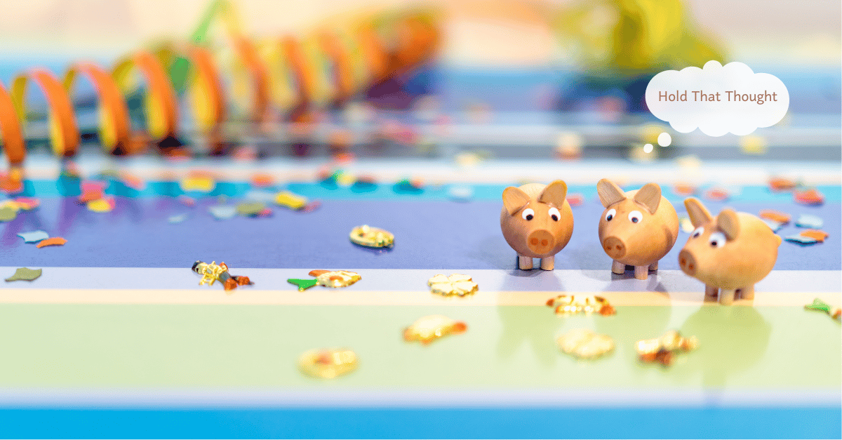 Three small wooden pigs are gathered on a colourful tabletop.