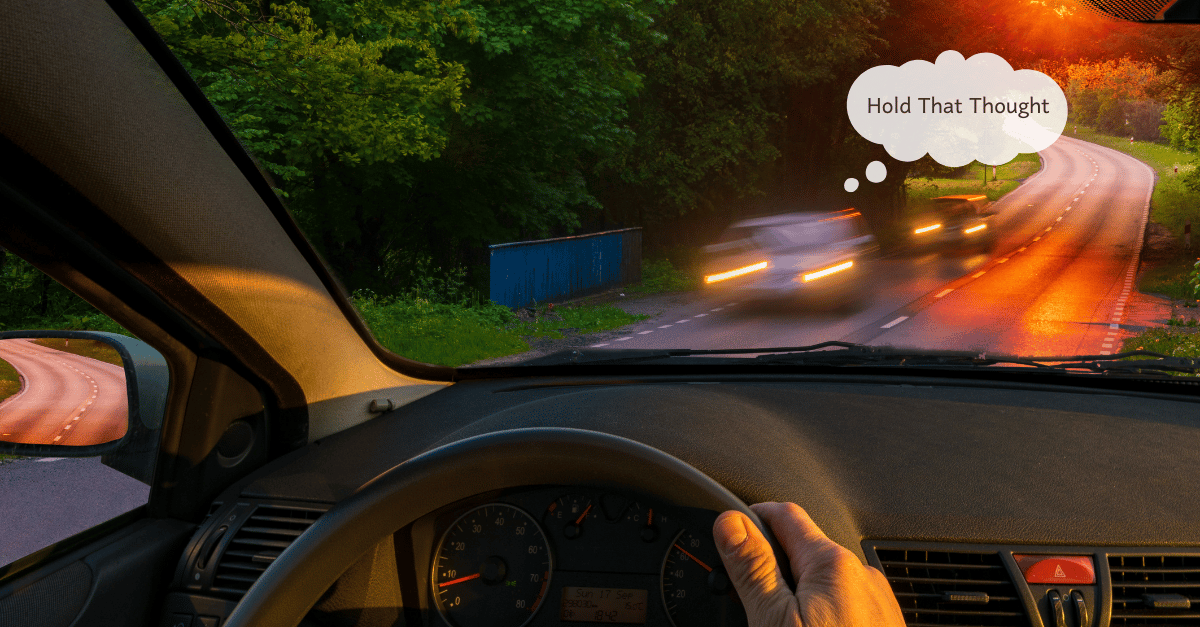 Hand on steering wheel of left-side drive car. View out window is of two cars passing quickly as the sun sets. Hold That Thought bubble hovers over lead car.