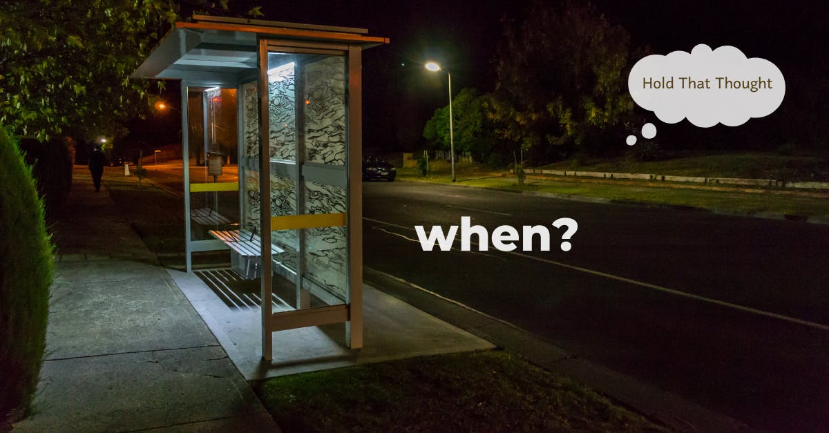 An empty bus stop at night, with the word 'when' written on the street in front of it.