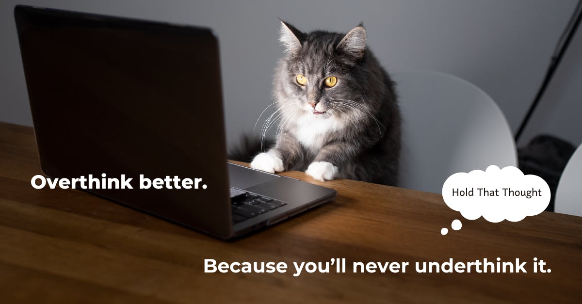 A perplexed cat sits at a desk, staring at a laptop screen. Text reads, “Overthink better. Because you'll never underthink it.”