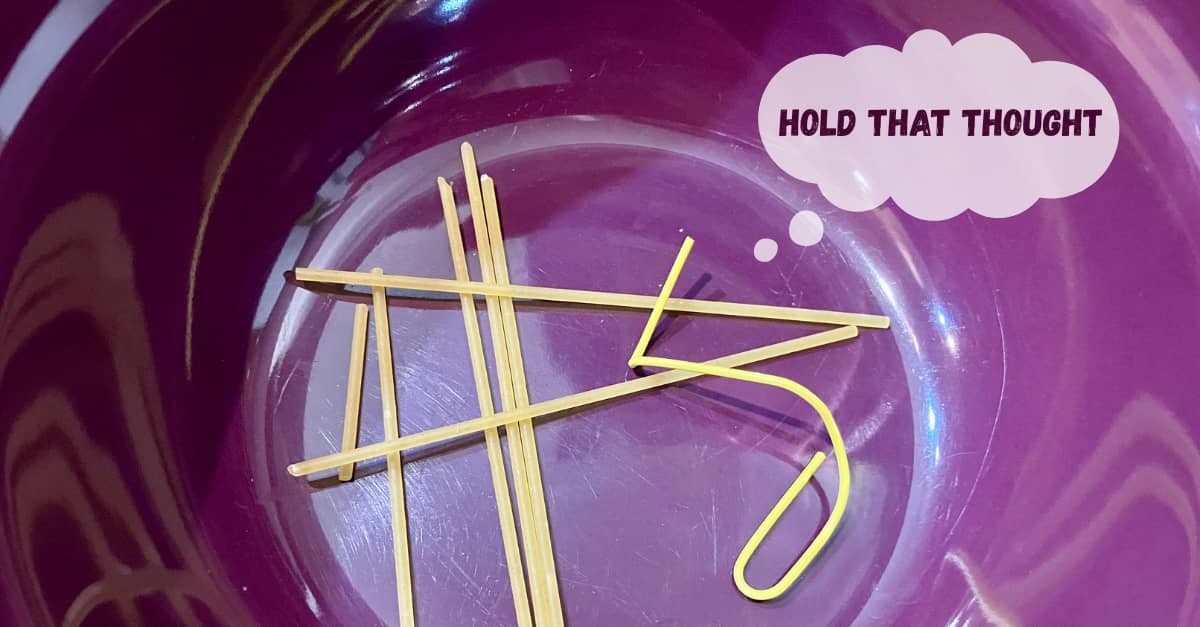 A close-up of a purple ceramic bowl with raw spaghetti and a bent paperclip.