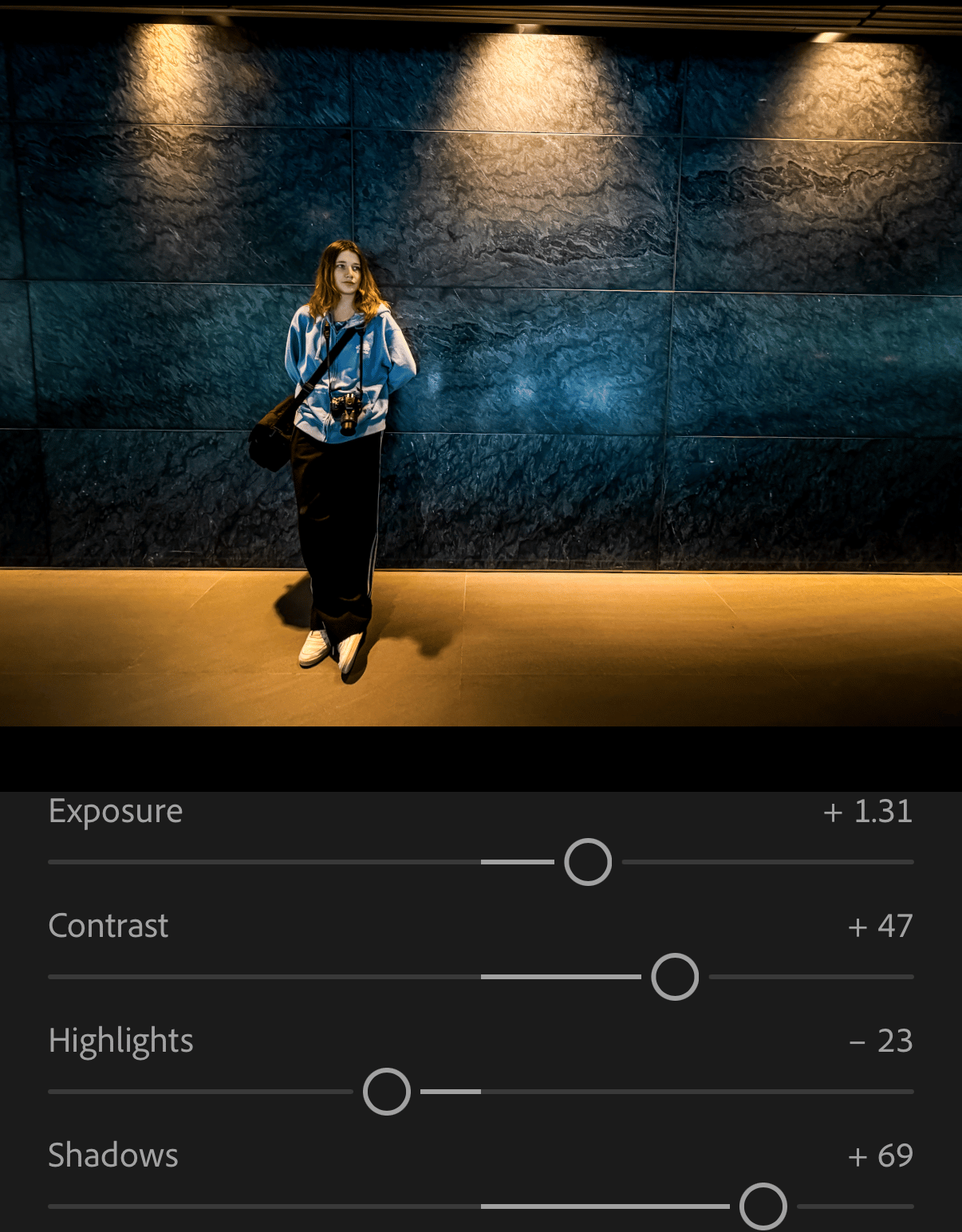 A screenshot of a photo of a girl standing against a wall, showing settings Lightroom how brightness and contrast was boosted.