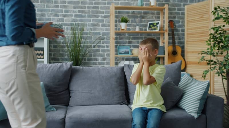 Child hides face while adult stands nearby.