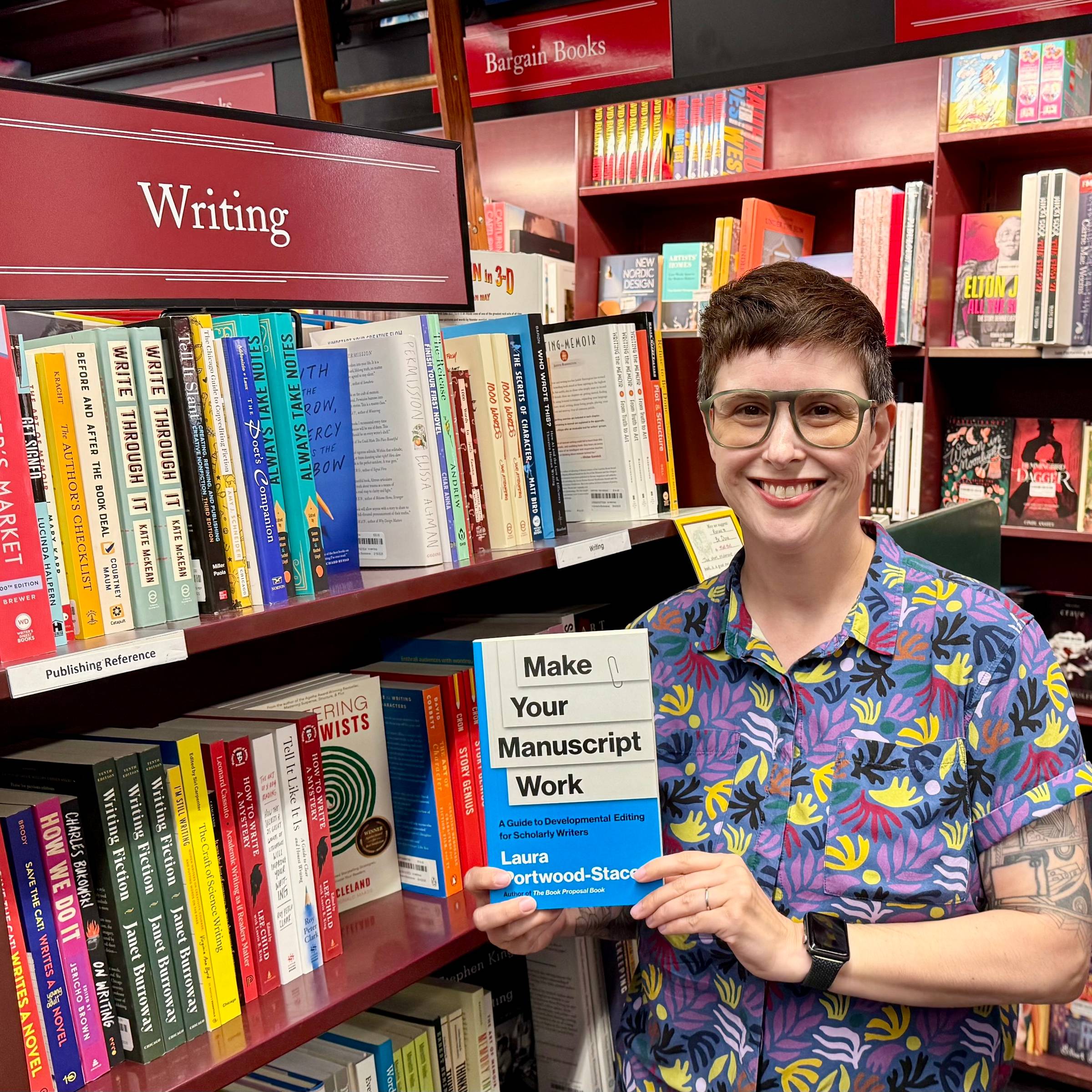 Me, standing in front of a bookstore shelf labeled "Writing" smiling and holding up a pcopy of Make Your Manuscript Work