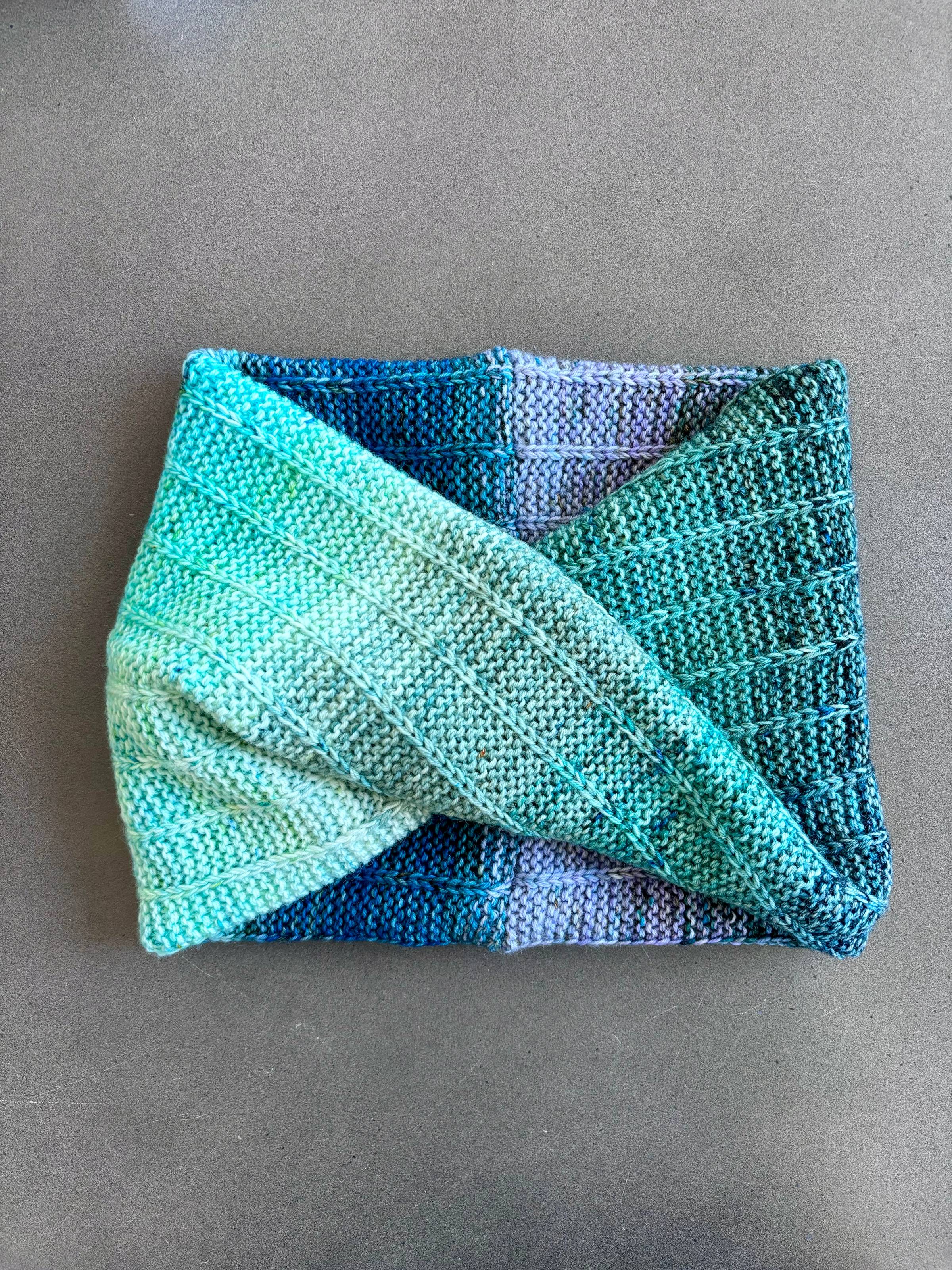 A knitted neck wrap with gradient colors from lavender to aqua to blue