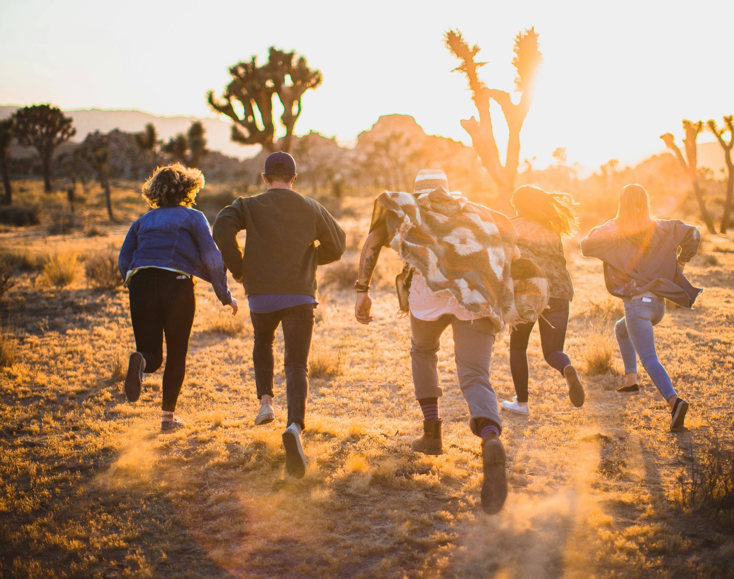 Group of friends running together through a desert landscape at golden hour