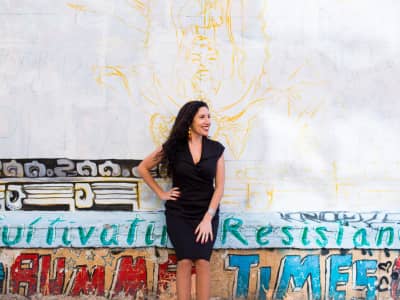 Maritza Schafer in a black dress smiling in front of a vibrant graffiti mural wall