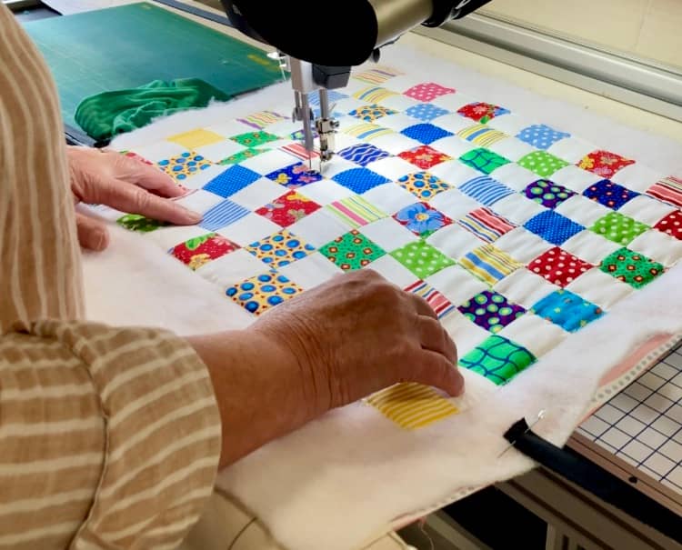 Image of a small quilt on a longarm frame with a set of hands on the quilt