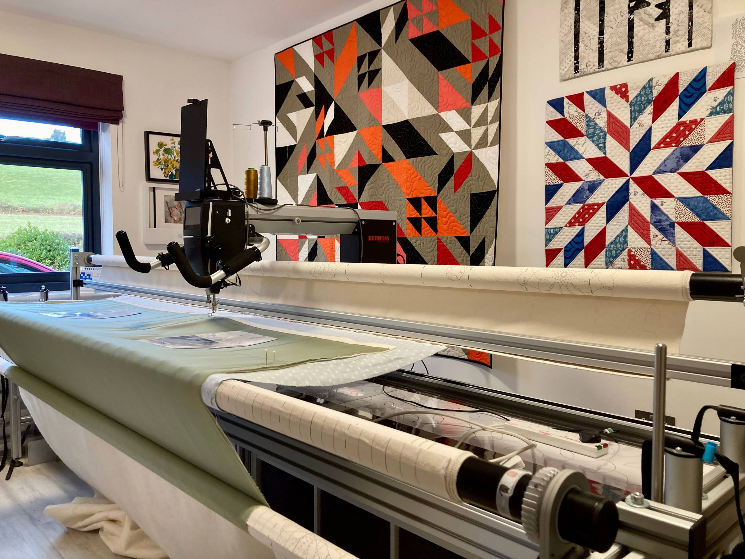 Image of a quilting machine with quilts hanging behind it.