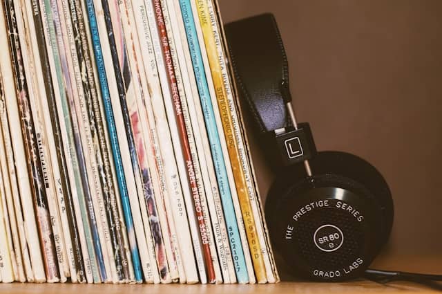Collection of music records on a shelf with over-the-ear headphones leaning against them.