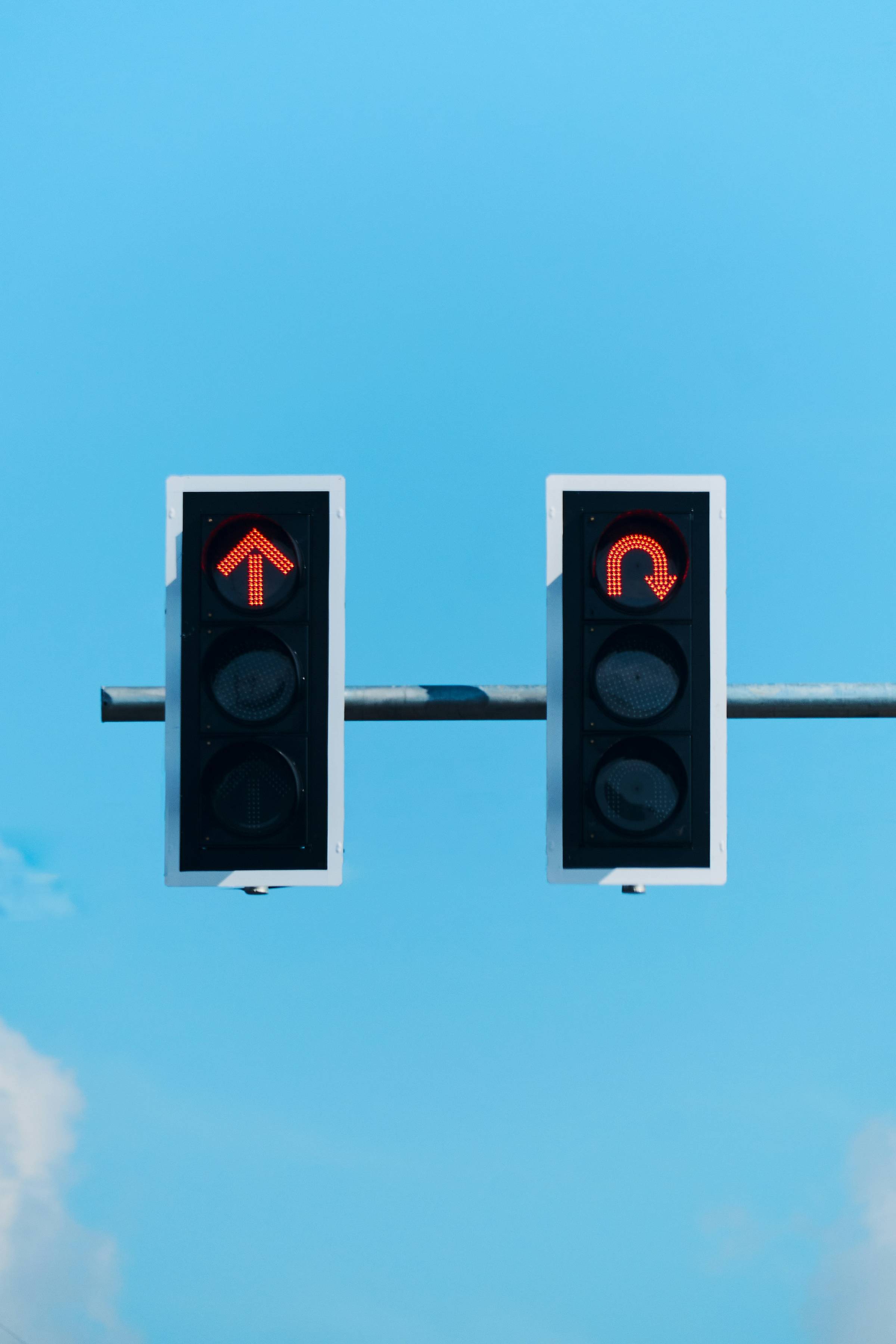 Two traffic lights against a blue sky. Left arrow pointing forward and right arrow indicating u-turn.