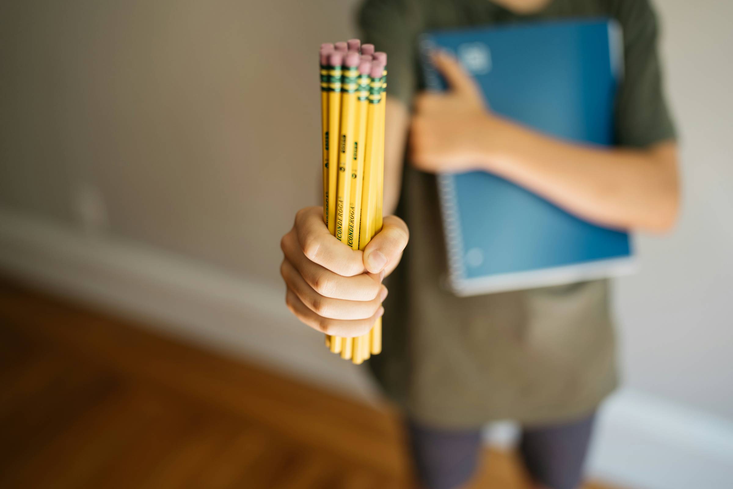 Bundle of yellow pencils held forward in focus, child and spiral notebook blurred in the background.