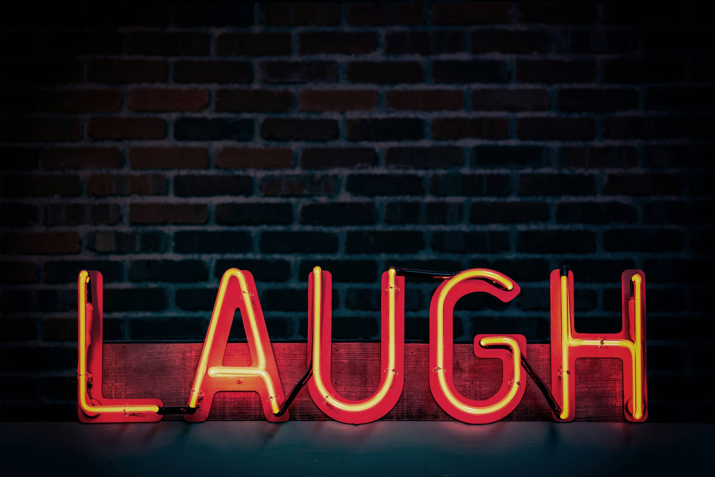 Orange neon sign spelling LAUGH in block capitals against a dark brick wall.