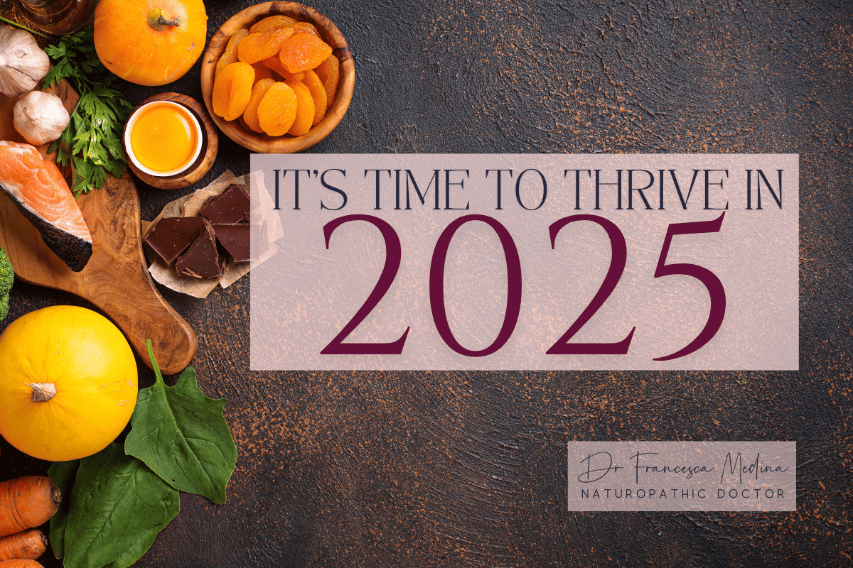 A variety of natural foods including salmon, dark chocolate, garlic, fresh greens, apricots, and squash are arranged on a dark textured background. Text over the image reads "It's time to thrive in 2025" in large, elegant font. A small box in the bottom r