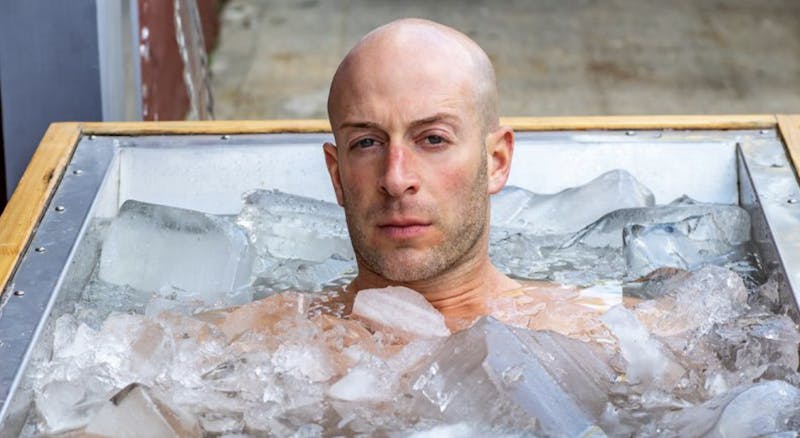 Photo of Josh York in an outdoor tub filled with large chunks of ice, as he gazes at the camera looking stoic.