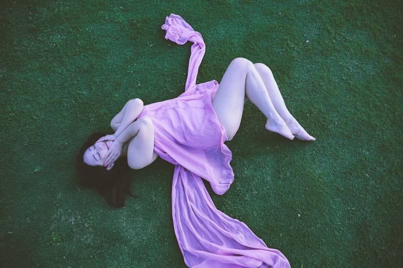 A person lies on green ground draped in pink fabric.