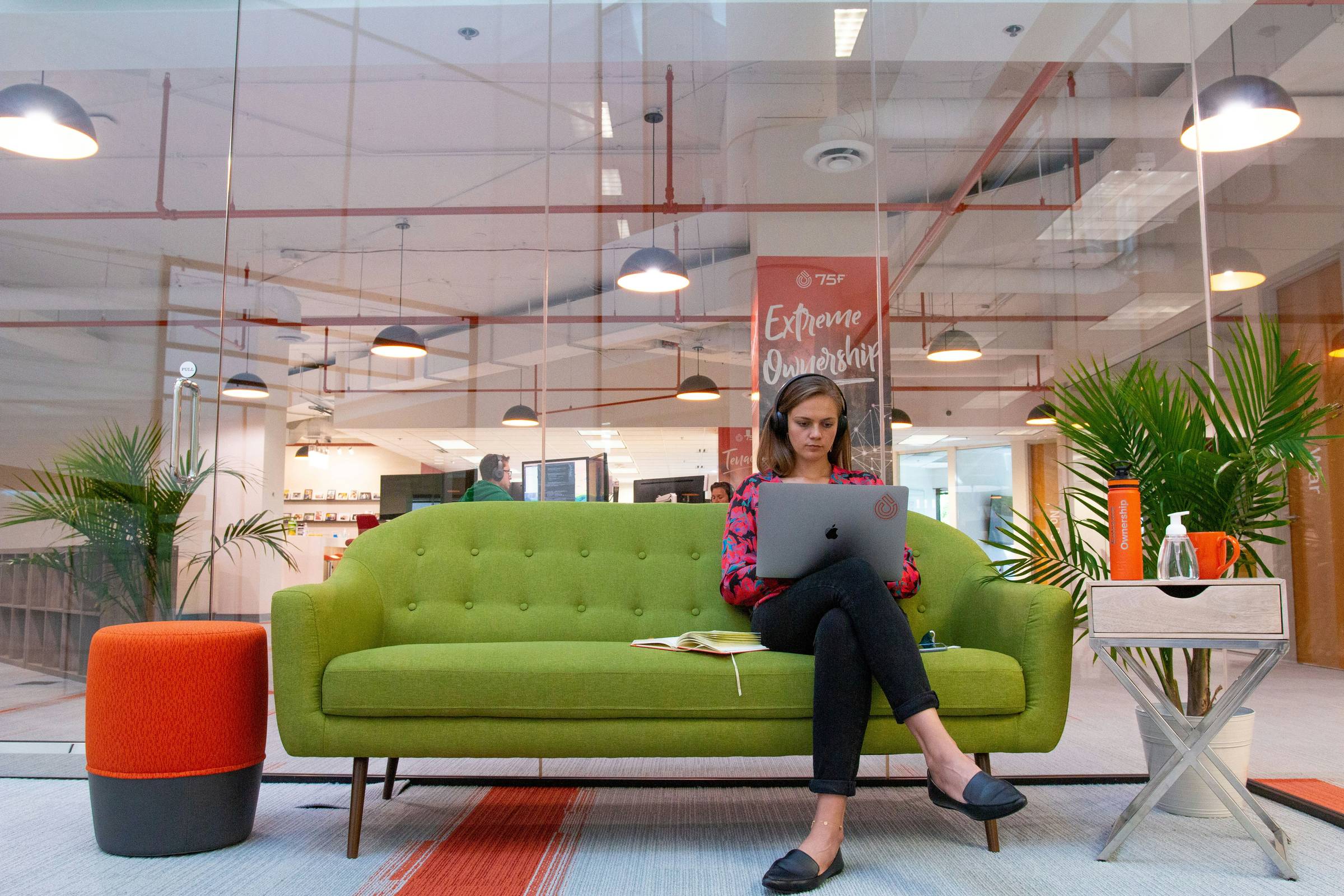 Woman typing on a green couch in the workplace
