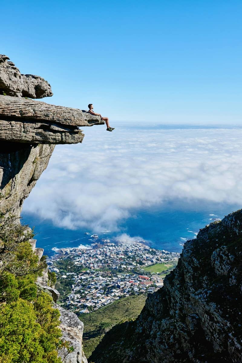 Person sitting on a cliff edge above clouds