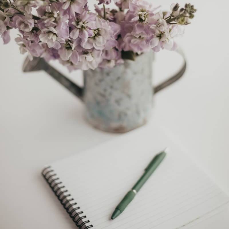 Flowers and a notebook sit on a white table.