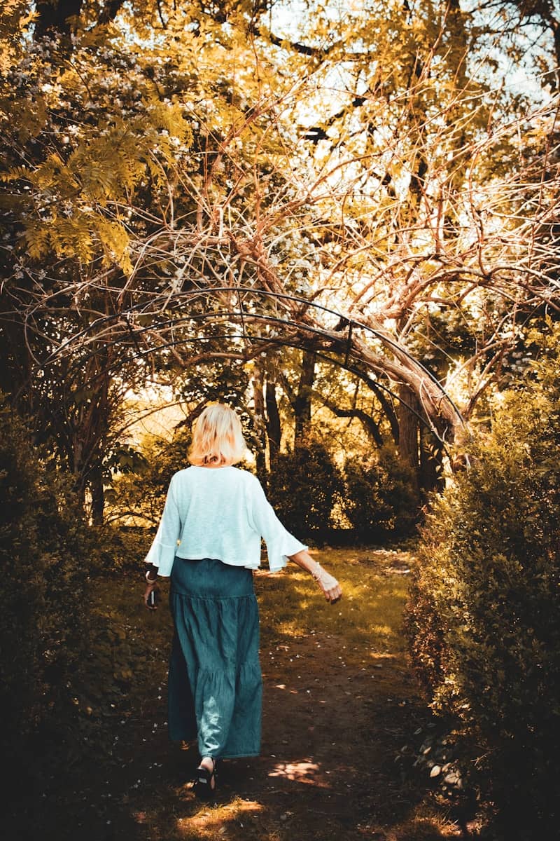 Woman walks through a sunlit garden archway.