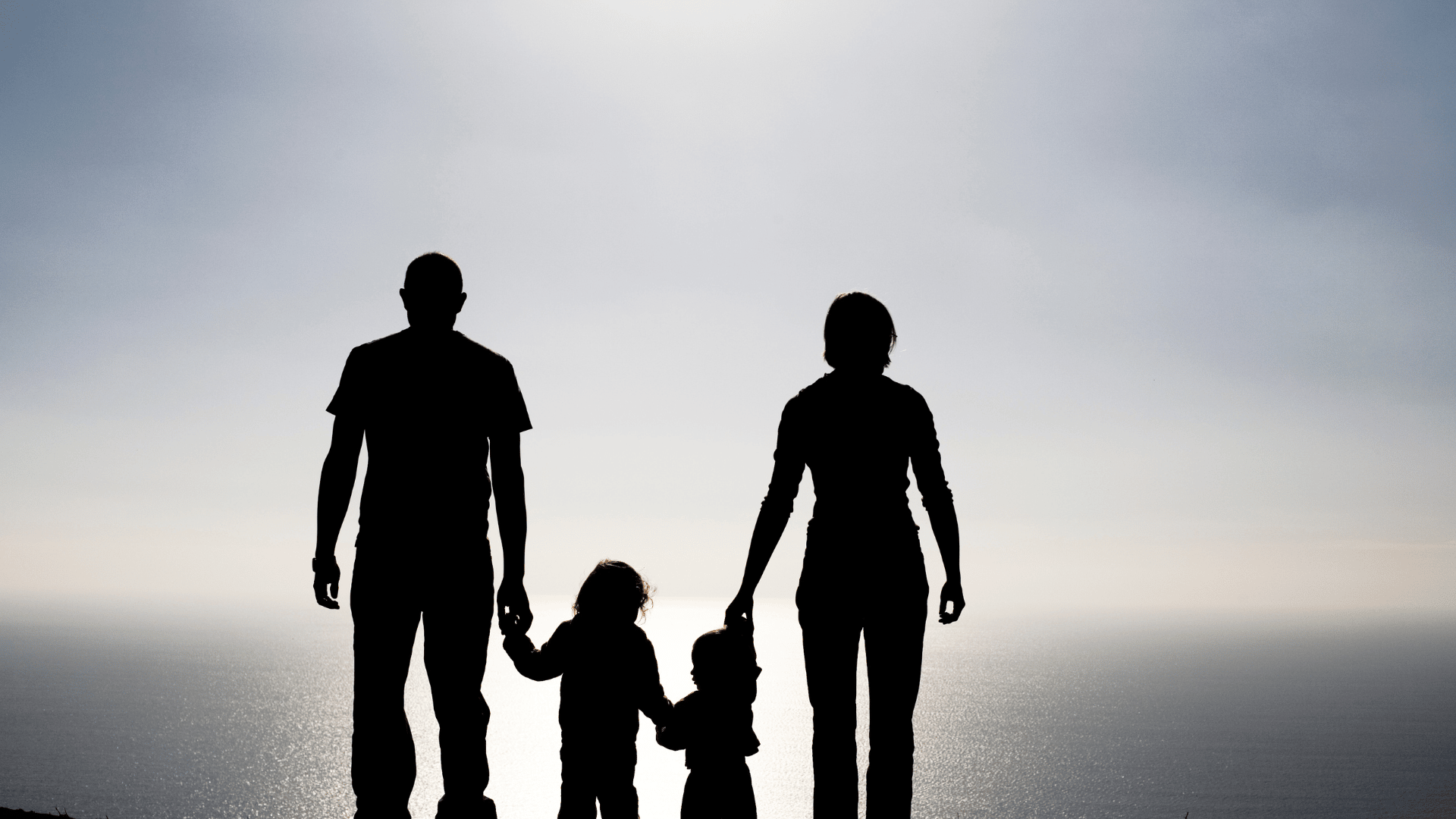 ID: A silhouette of a family with the ocean at their backs