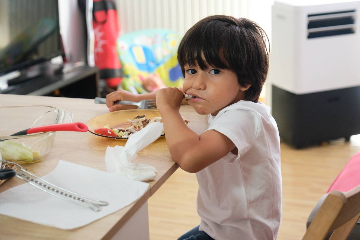 A little boy with a plate in front of him and his fingers in his mouth