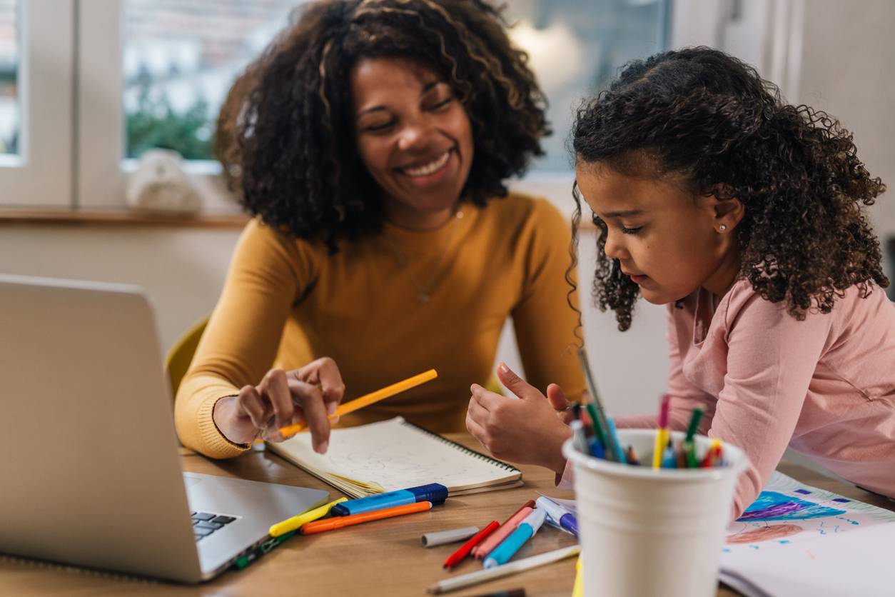 A mother engaging her daughter, while letting the work on her laptop take a backseat to connection with her 4 to 5 year old daugther. 