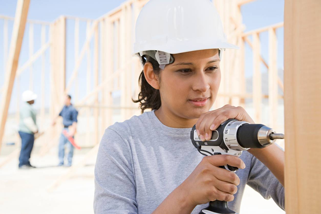 A young woman is drilling at a construction site with her helmet on.