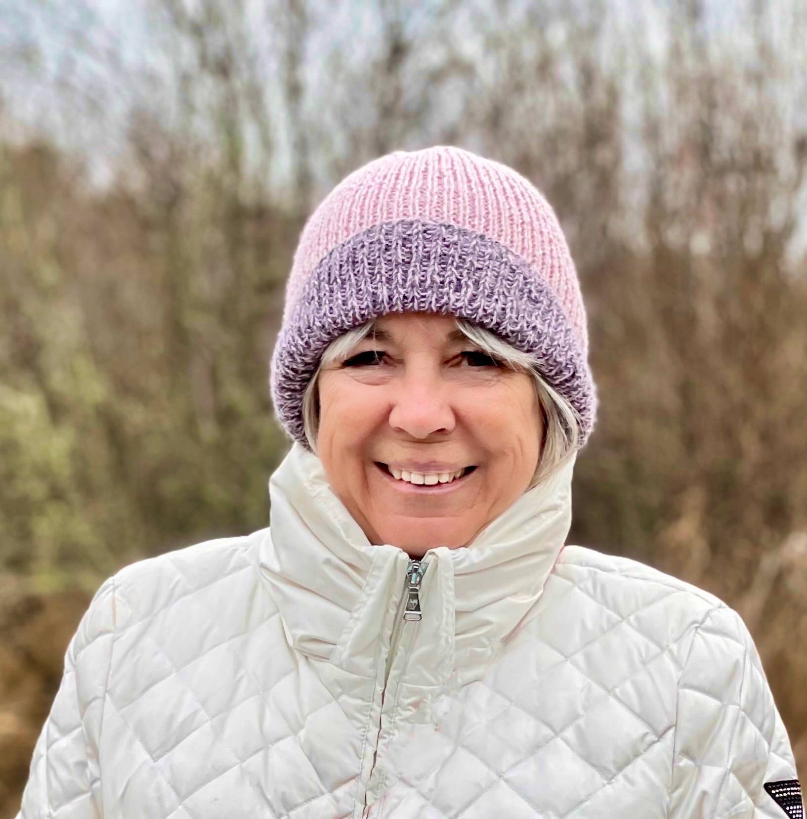 A photo of Bonnie from 2024 wearing a pink and purple wool hat with a white puffy jacket. She is smiling.