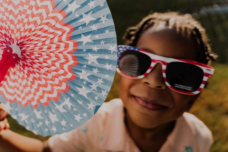 A child celebrates with patriotic sunglasses and a fan.