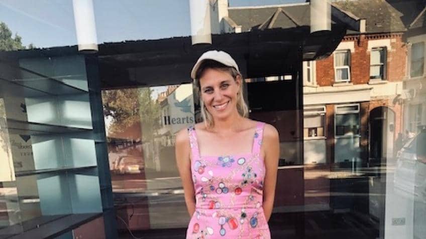 woman in pink dress and cap smiling outside not-yet-a-coffee-shop
