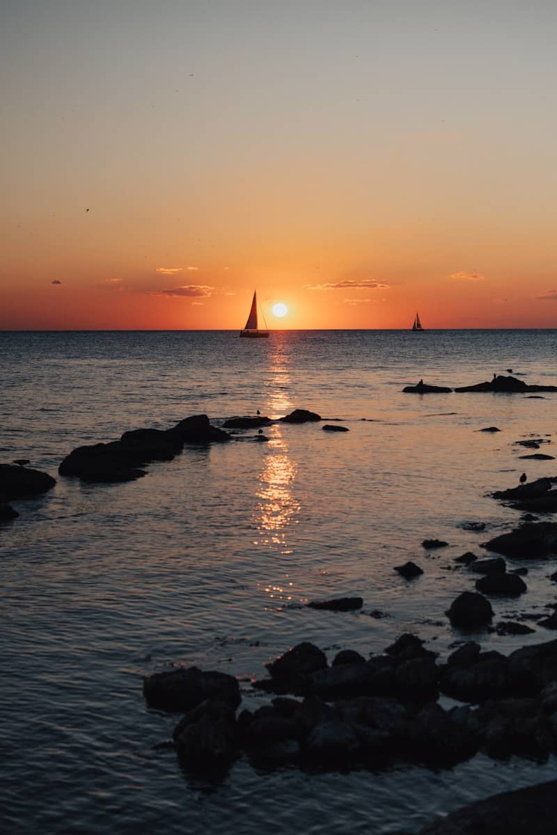 The sun is setting over the ocean with a sailboat in the distance