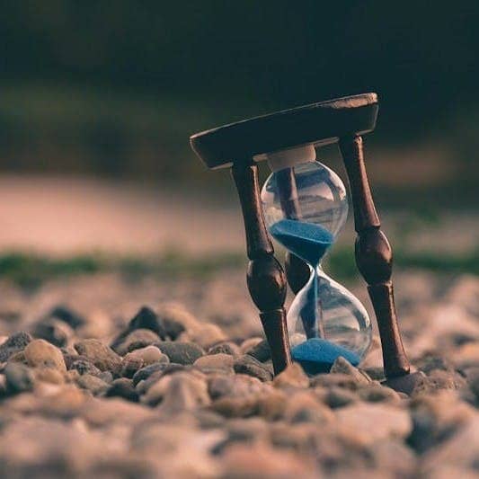 selective focus photo of brown and blue hourglass on stones