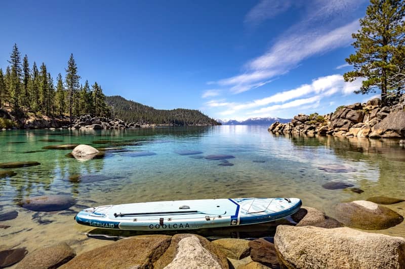 Serene lake with paddleboard, clear water, and distant pine forests.