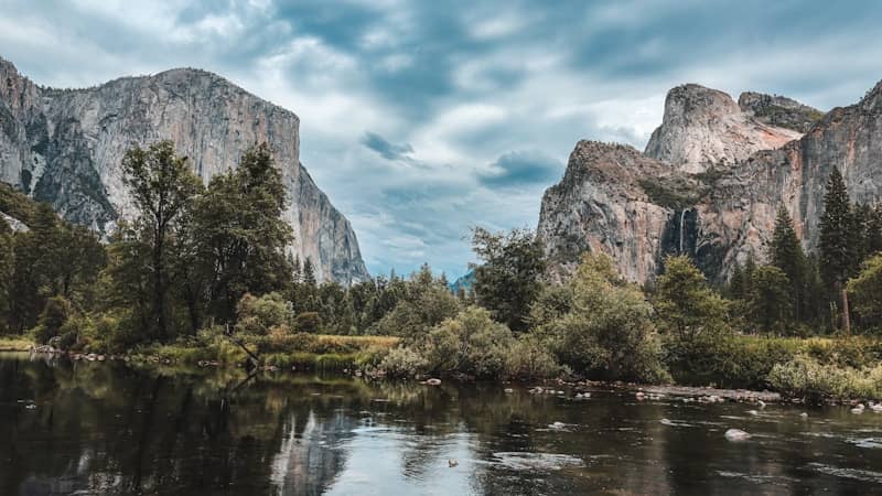 Majestic mountains and river with trees under a cloudy sky.