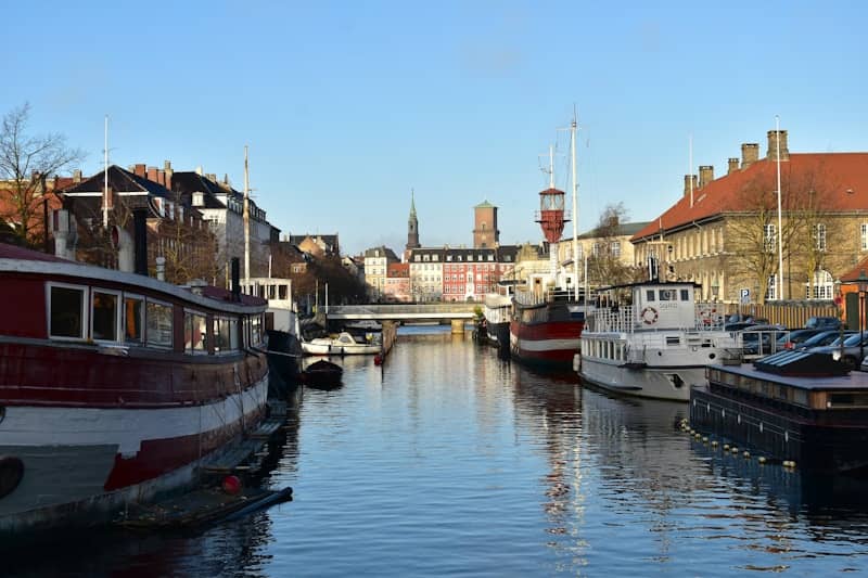 Boats docked along a canal with buildings and bridge.