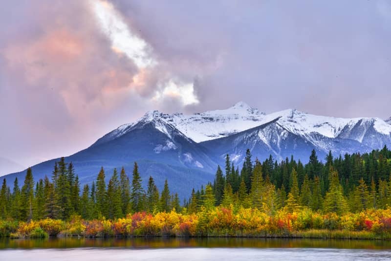 Snow-covered mountains, colorful autumn trees, and a tranquil lake.