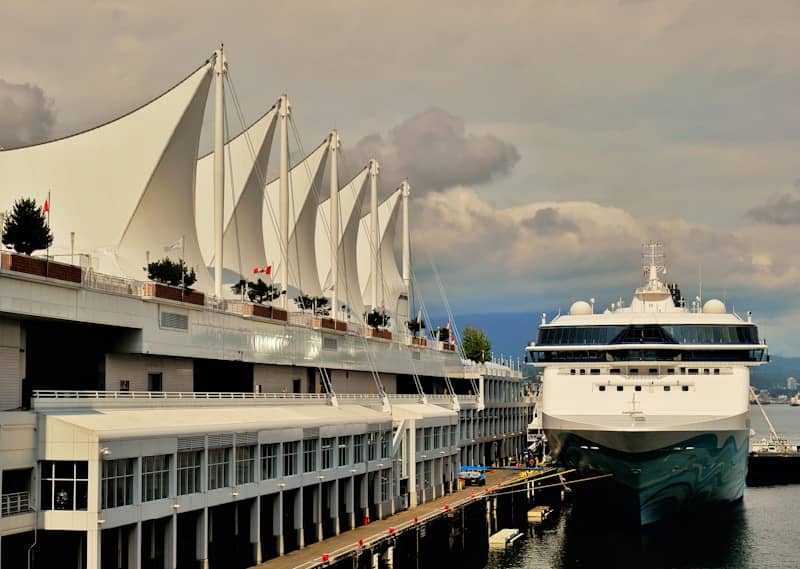 Cruise ship docked at a modern building with sail-like roof.