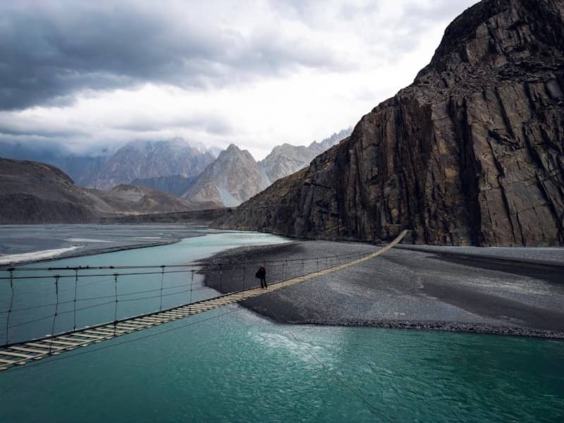 A man walking across a suspension bridge over a river