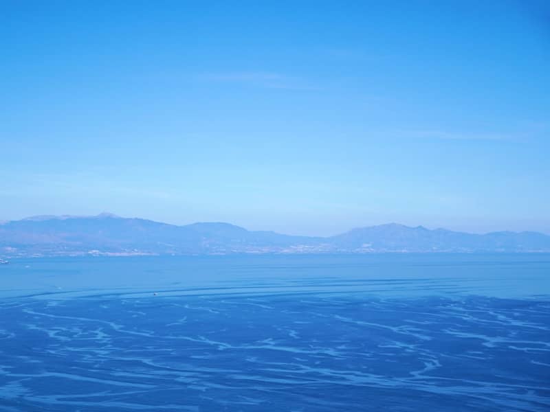 Calm blue ocean water with distant mountains under clear sky