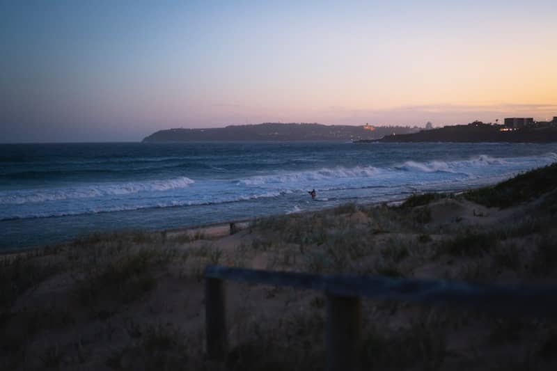 Ocean waves crash on a sandy beach at dusk.