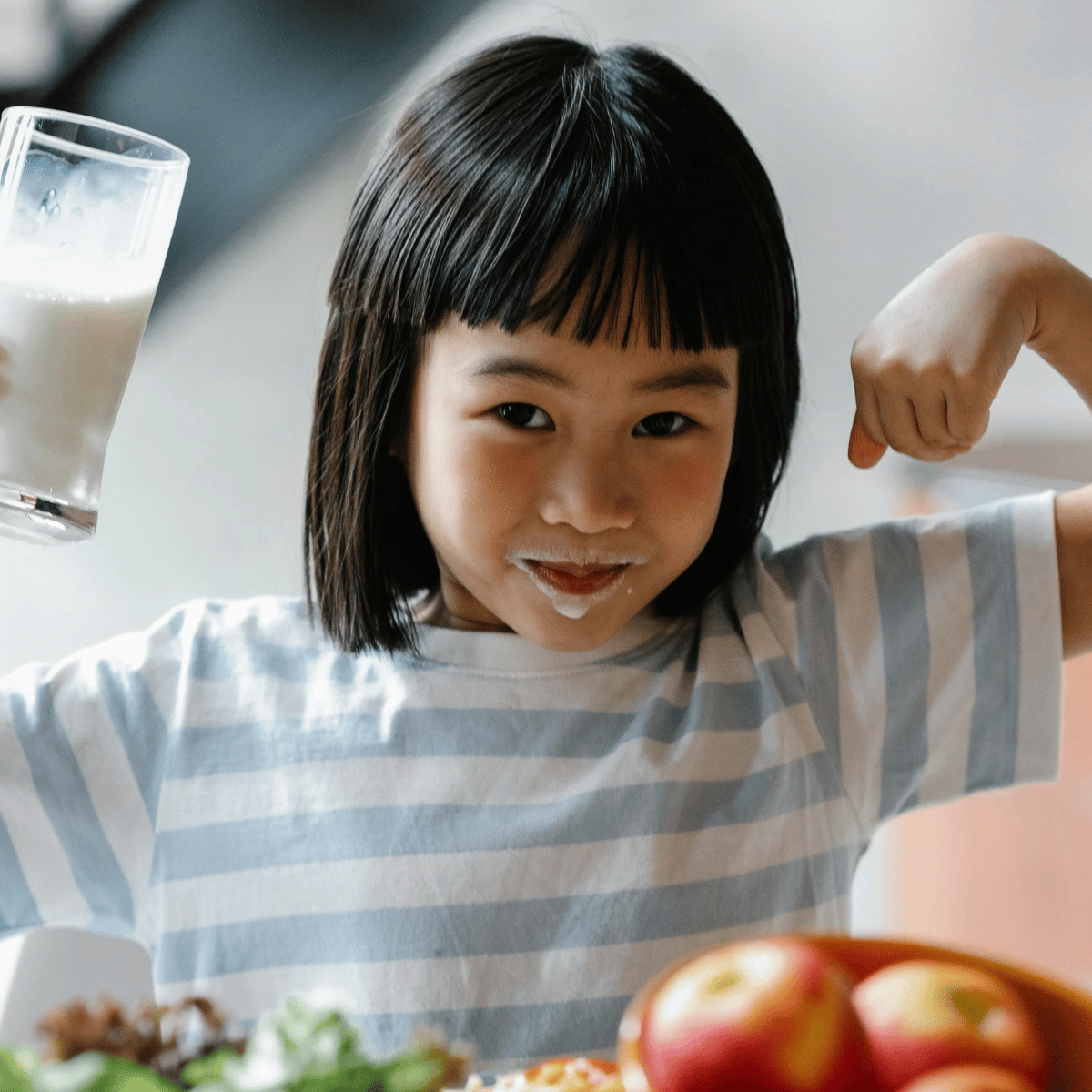 Girl Holding Up Arms to Show Muscles While Drinking Milk